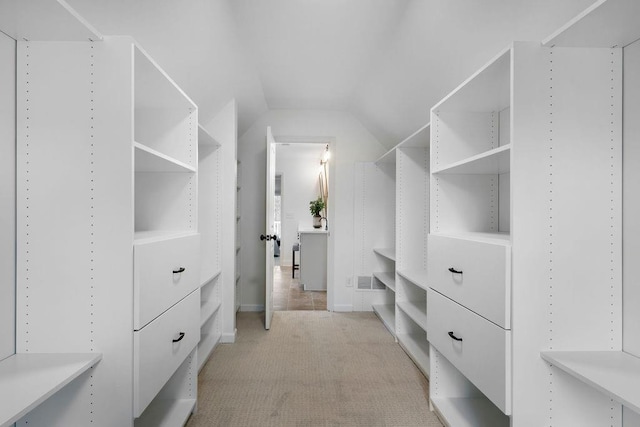 walk in closet with vaulted ceiling and light colored carpet