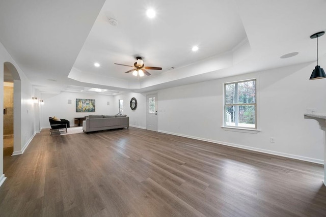 unfurnished living room with dark hardwood / wood-style floors, ceiling fan, and a tray ceiling