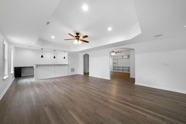 unfurnished living room with a tray ceiling, dark wood-type flooring, and ceiling fan