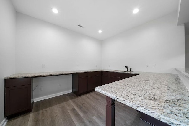 kitchen featuring sink, dark wood-type flooring, light stone counters, built in desk, and kitchen peninsula