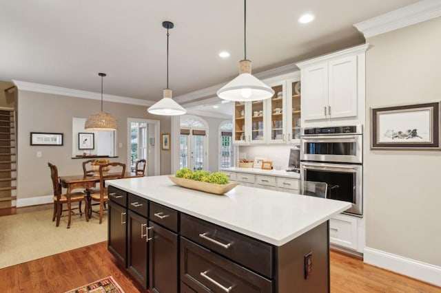 kitchen with decorative light fixtures, light hardwood / wood-style floors, ornamental molding, double oven, and a kitchen island