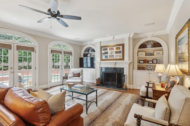 living room with hardwood / wood-style floors, a fireplace, built in shelves, french doors, and ceiling fan