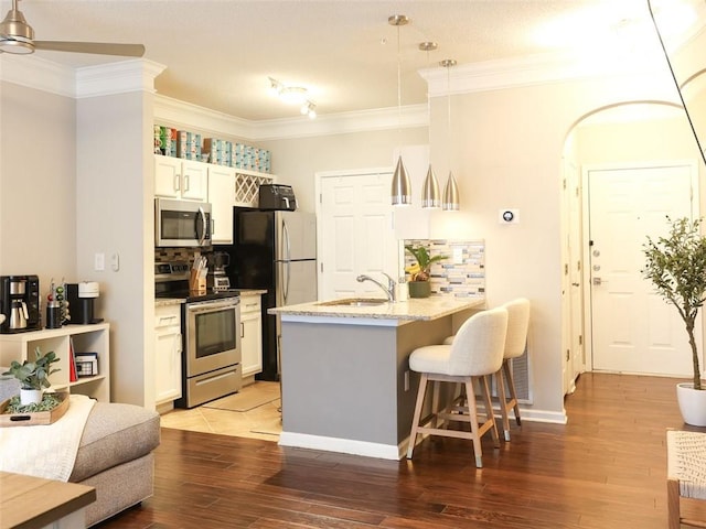 kitchen with appliances with stainless steel finishes, decorative light fixtures, white cabinetry, sink, and light stone counters