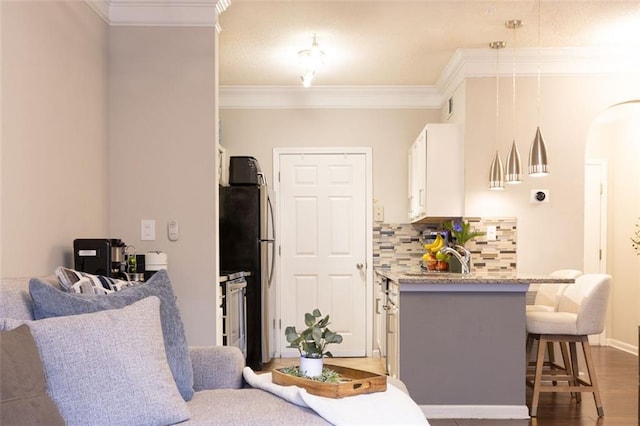 kitchen featuring stainless steel refrigerator, ornamental molding, light stone countertops, decorative backsplash, and white cabinets