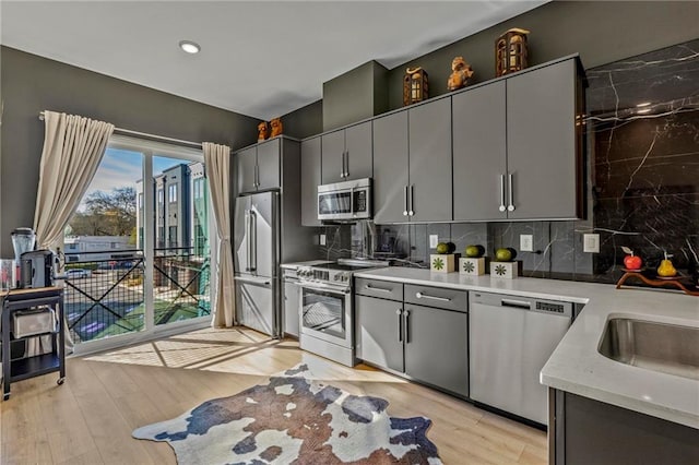 kitchen featuring gray cabinetry, tasteful backsplash, stainless steel appliances, and light wood-type flooring