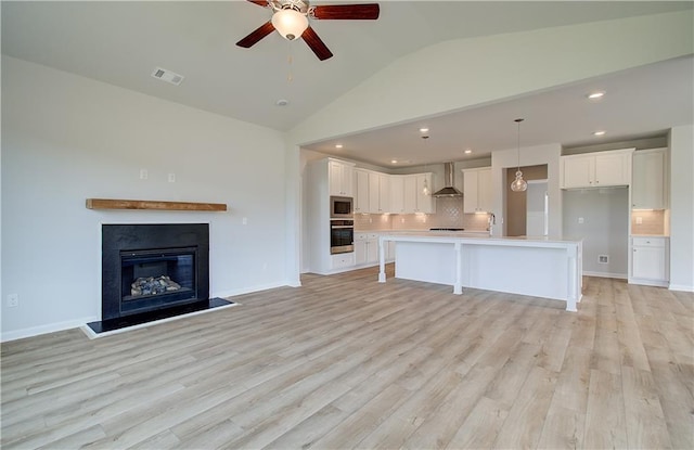 kitchen featuring white cabinetry, wall chimney range hood, a kitchen island with sink, and appliances with stainless steel finishes