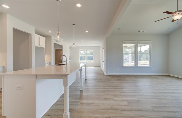 kitchen with decorative light fixtures, white cabinetry, sink, a breakfast bar area, and a large island