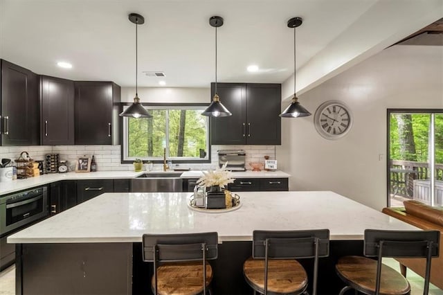 kitchen with wall oven, backsplash, a center island, a sink, and a kitchen bar