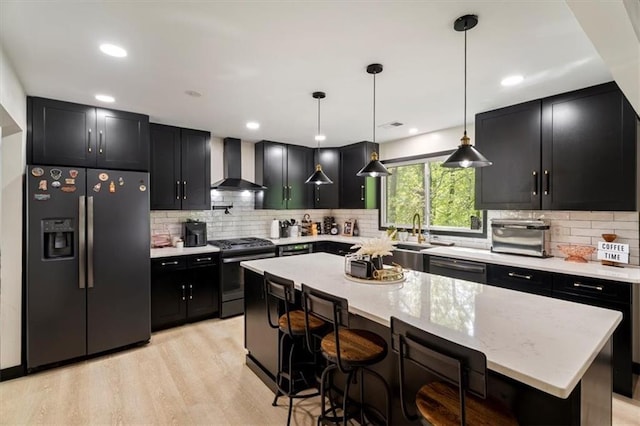 kitchen featuring refrigerator with ice dispenser, range with gas stovetop, wall chimney range hood, dark cabinetry, and recessed lighting