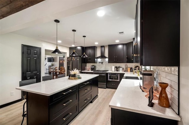 kitchen with gas stove, wall chimney range hood, refrigerator with ice dispenser, tasteful backsplash, and dark cabinetry
