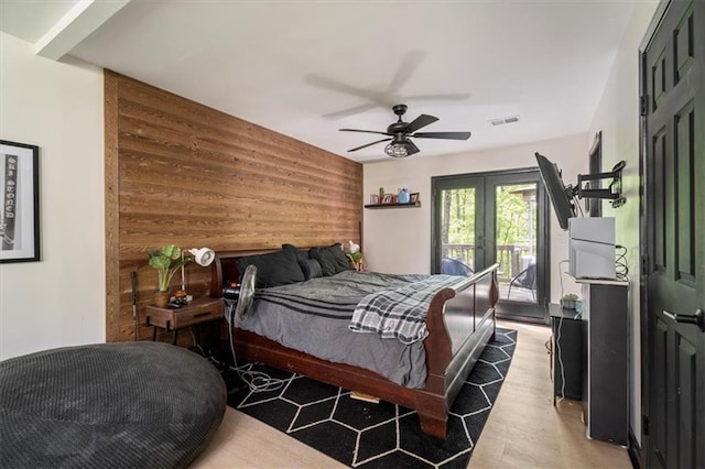 bedroom featuring access to exterior, light wood finished floors, wood walls, a ceiling fan, and french doors