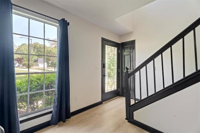foyer entrance featuring stairway, baseboards, and light wood finished floors