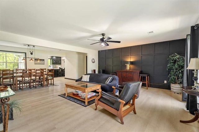 living room with a decorative wall, a ceiling fan, and light wood-type flooring