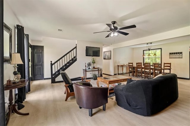 living area with stairway, a ceiling fan, and light wood finished floors