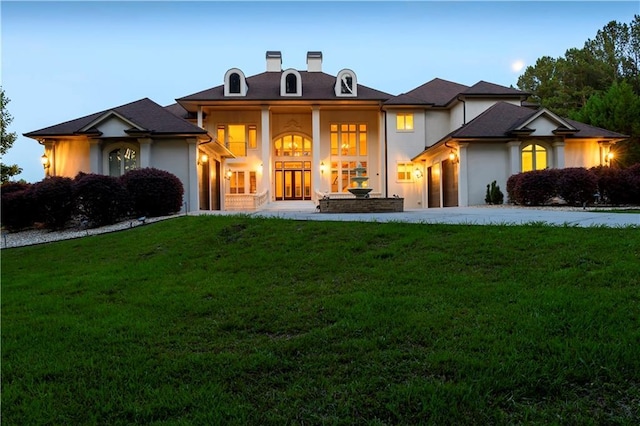 back of house with an attached garage, driveway, a chimney, and a lawn