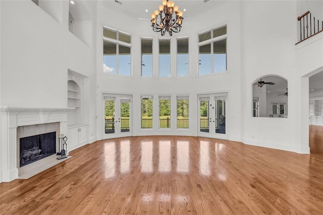 unfurnished living room featuring built in features, a tile fireplace, french doors, and light wood finished floors