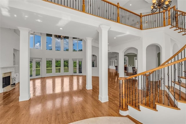 interior space featuring a notable chandelier, a fireplace with flush hearth, a towering ceiling, light wood-style floors, and stairway