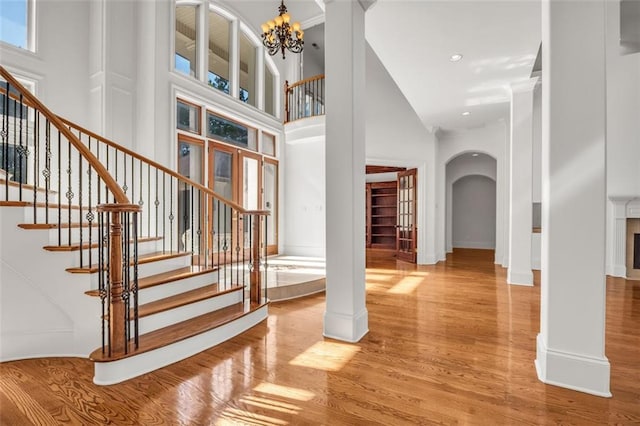 entrance foyer with light wood finished floors, arched walkways, stairs, a high ceiling, and a notable chandelier