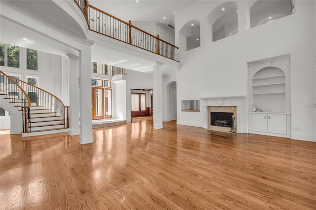 unfurnished living room featuring built in features, a fireplace, stairway, a high ceiling, and light wood-type flooring