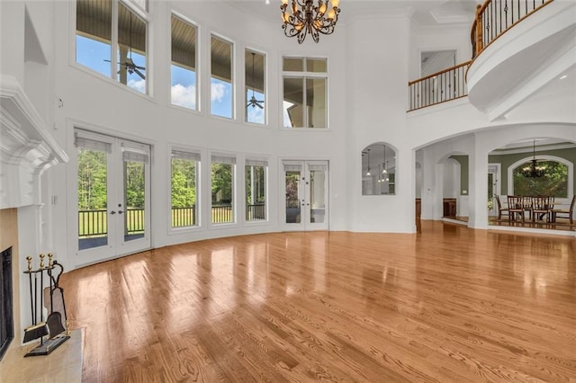 unfurnished living room with arched walkways, wood finished floors, french doors, a fireplace, and a chandelier