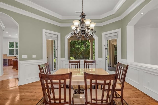 dining space with arched walkways, wainscoting, and light wood-style flooring