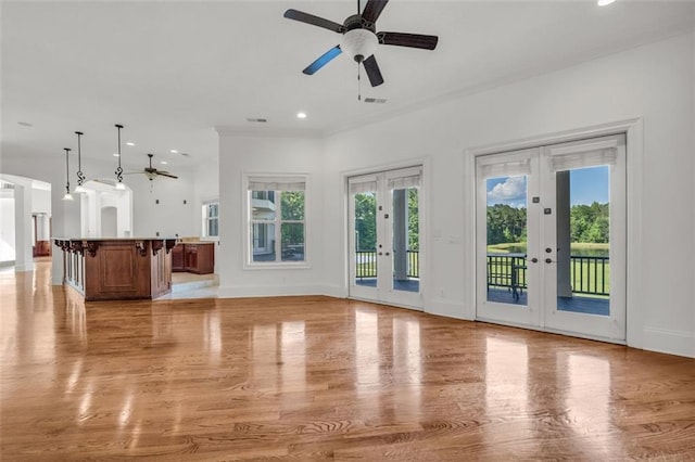 unfurnished living room featuring ceiling fan, french doors, arched walkways, and baseboards