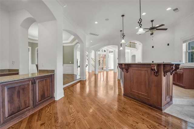 kitchen featuring a breakfast bar, arched walkways, hanging light fixtures, light wood-style flooring, and ornamental molding