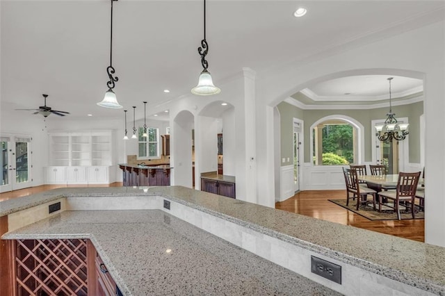 kitchen featuring light stone counters, a decorative wall, a wainscoted wall, decorative light fixtures, and crown molding