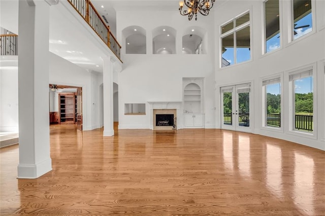 unfurnished living room featuring light wood-type flooring, a chandelier, built in features, and a high end fireplace