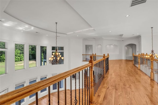 corridor with a tray ceiling, light wood-style flooring, visible vents, and a notable chandelier