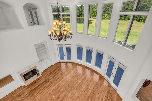 unfurnished living room with a tiled fireplace, wood finished floors, a high ceiling, french doors, and a notable chandelier