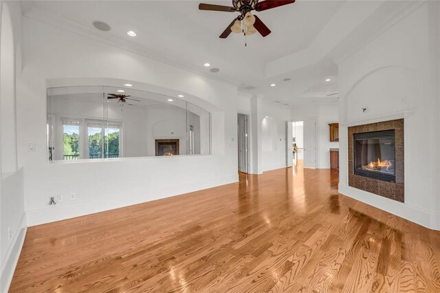 unfurnished living room with a ceiling fan, a tray ceiling, light wood-type flooring, a fireplace, and recessed lighting