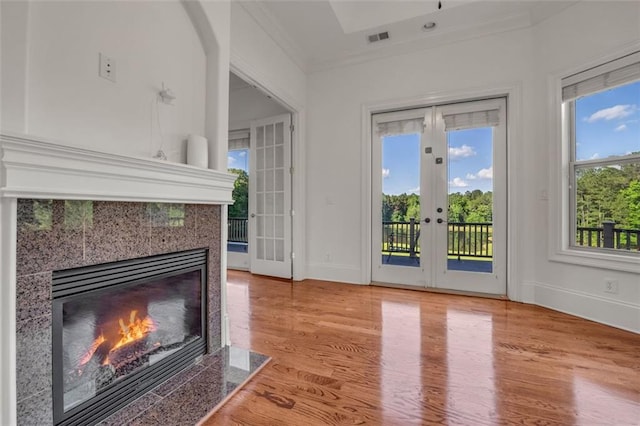 doorway featuring french doors, visible vents, light wood-style flooring, ornamental molding, and a tile fireplace