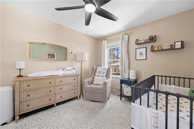 bedroom featuring a nursery area, ceiling fan, and light carpet