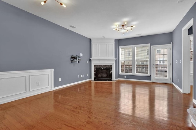 unfurnished living room with a high end fireplace, visible vents, baseboards, an inviting chandelier, and wood finished floors