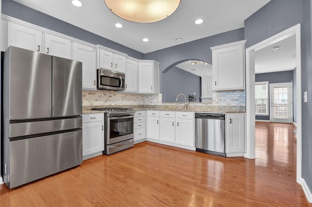 kitchen with light wood finished floors, tasteful backsplash, appliances with stainless steel finishes, arched walkways, and white cabinetry