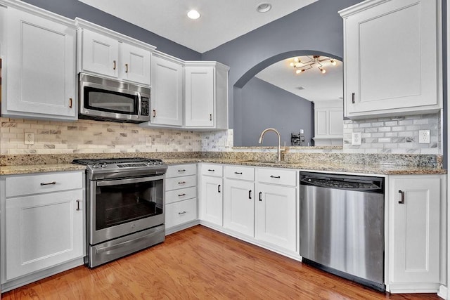 kitchen with a sink, white cabinetry, stainless steel appliances, arched walkways, and light wood-style floors