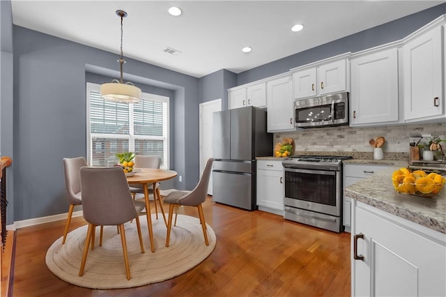 kitchen with visible vents, stainless steel appliances, decorative backsplash, white cabinets, and light wood-style floors