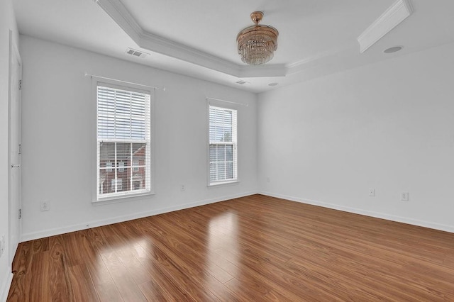 unfurnished room with visible vents, a raised ceiling, wood finished floors, and ornamental molding