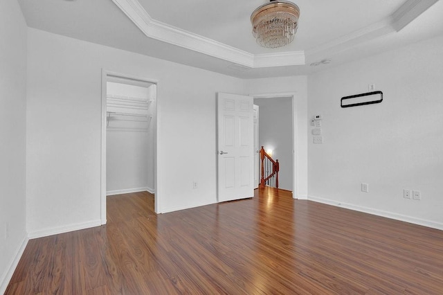 unfurnished bedroom featuring a spacious closet, baseboards, ornamental molding, wood finished floors, and a raised ceiling