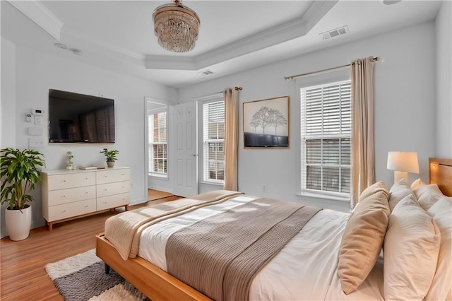 bedroom with a tray ceiling, light wood-style flooring, visible vents, and ornamental molding