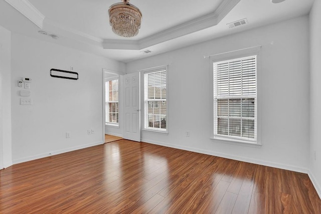 empty room featuring visible vents, wood finished floors, baseboards, crown molding, and a raised ceiling