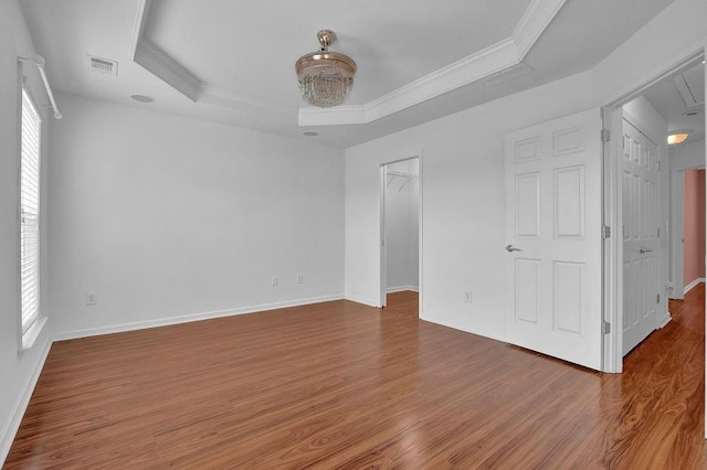 spare room with wood finished floors, baseboards, visible vents, ornamental molding, and a raised ceiling