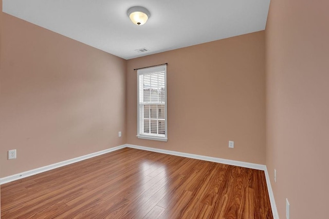 spare room with wood finished floors, visible vents, and baseboards