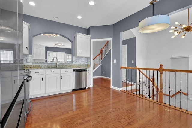 kitchen featuring light wood-type flooring, a notable chandelier, light stone counters, white cabinetry, and stainless steel appliances