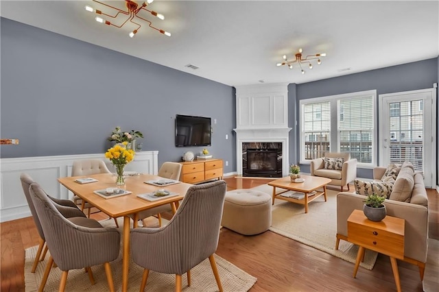 dining room with wood finished floors, visible vents, a premium fireplace, an inviting chandelier, and wainscoting