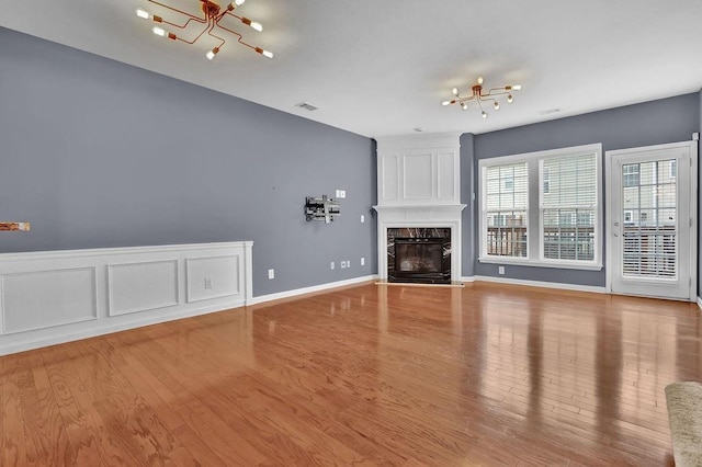 unfurnished living room featuring a high end fireplace, visible vents, a decorative wall, wood finished floors, and a notable chandelier