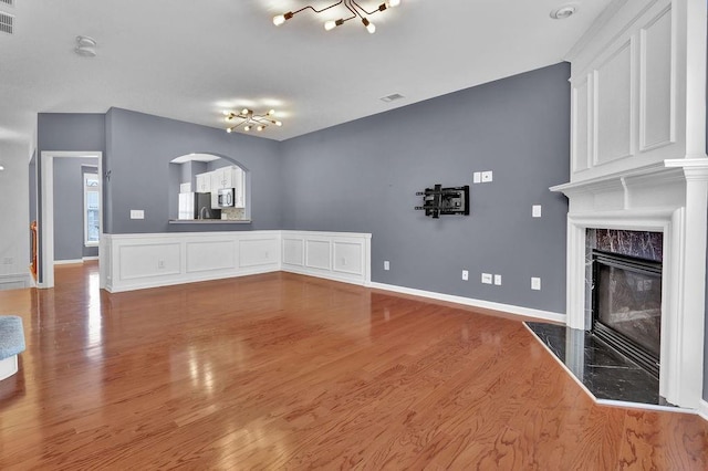 unfurnished living room featuring wood finished floors, visible vents, baseboards, a fireplace, and arched walkways