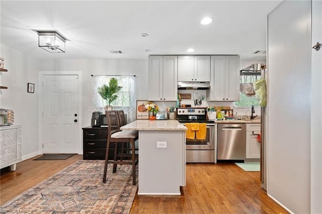 kitchen with light hardwood / wood-style floors, a kitchen island, a kitchen bar, light stone countertops, and stainless steel appliances