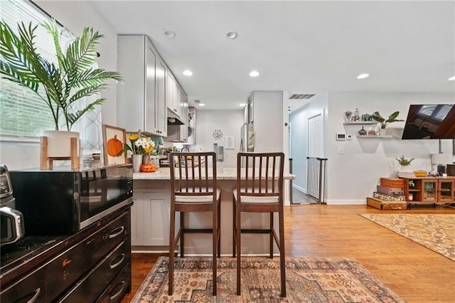 kitchen with light wood-type flooring, a breakfast bar area, white cabinets, and light stone counters